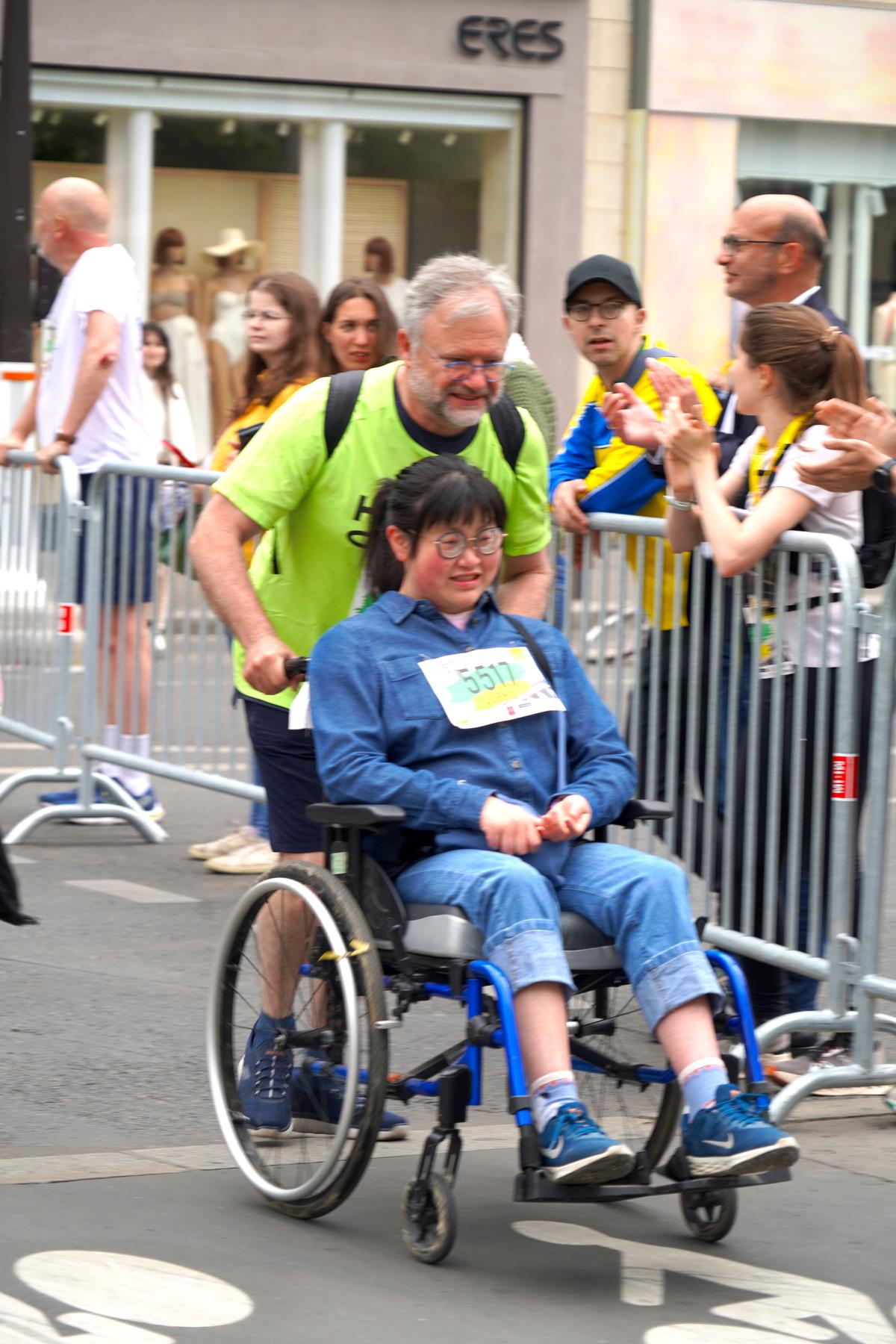 Une jeune fille en fauteuil roulant est poussée lors du Paris Eglises Tour 2025 par un coureur.