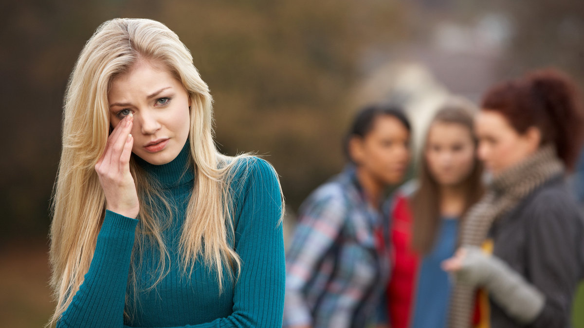 Upset Teenage Girl With Friends Gossiping In Background