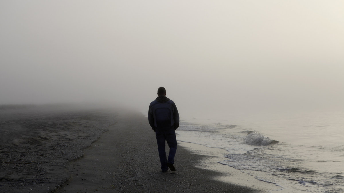 Lonely man walking on a foggy beach