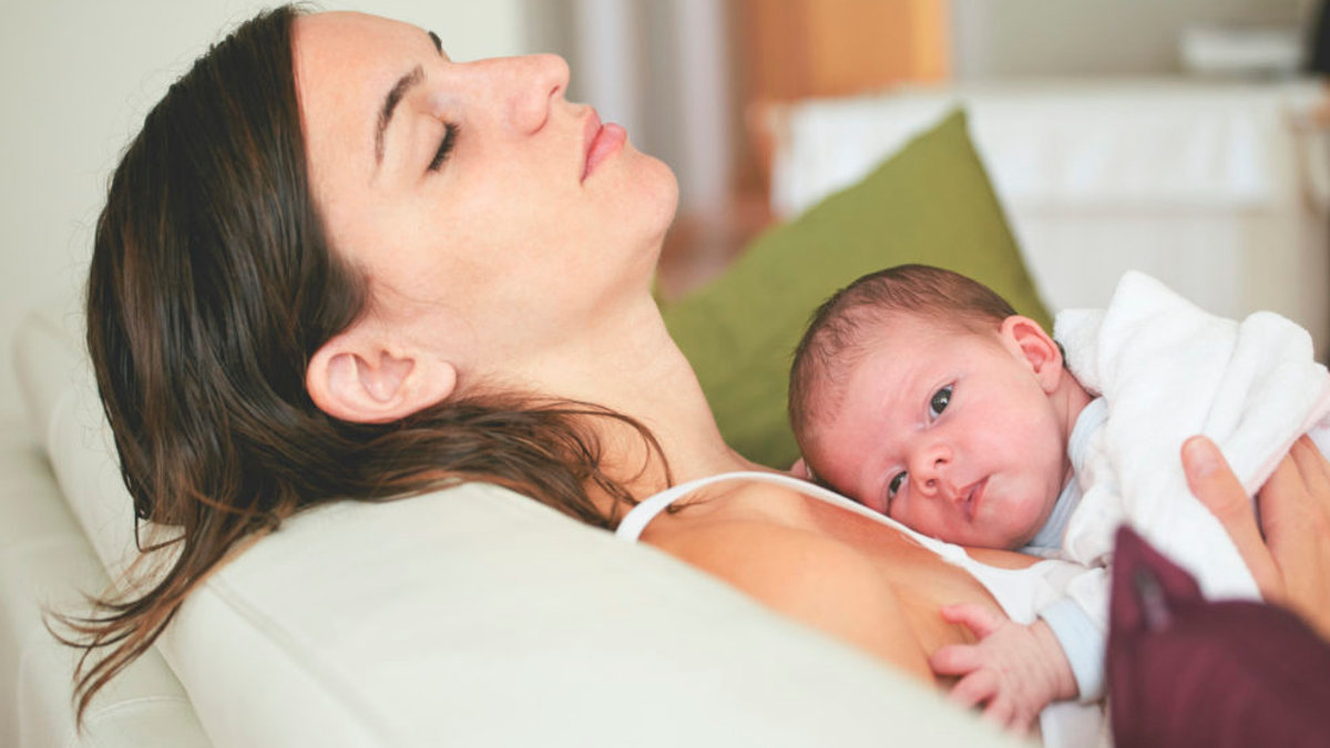 Tired mom sleeping on couch with cute baby in her arms.