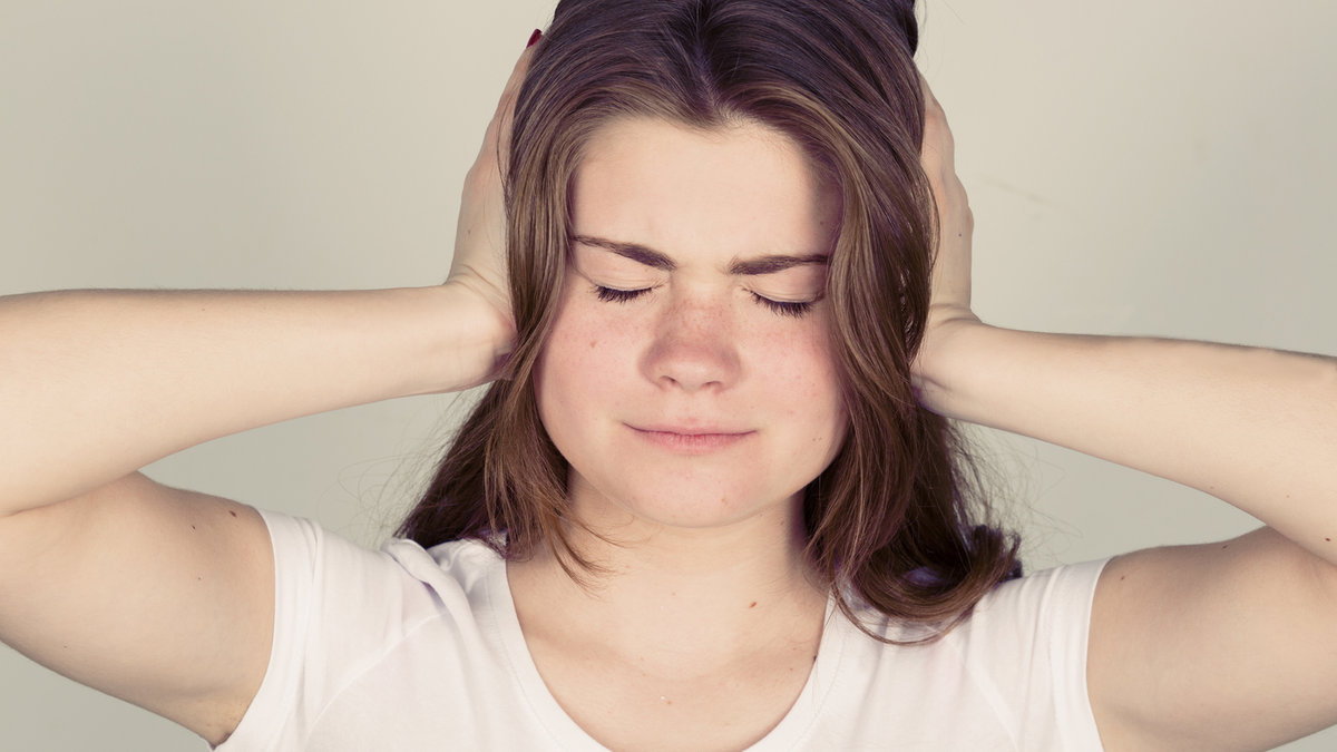 Too loud sound. Teenage girl covering ears with hands and keeping eyes closed