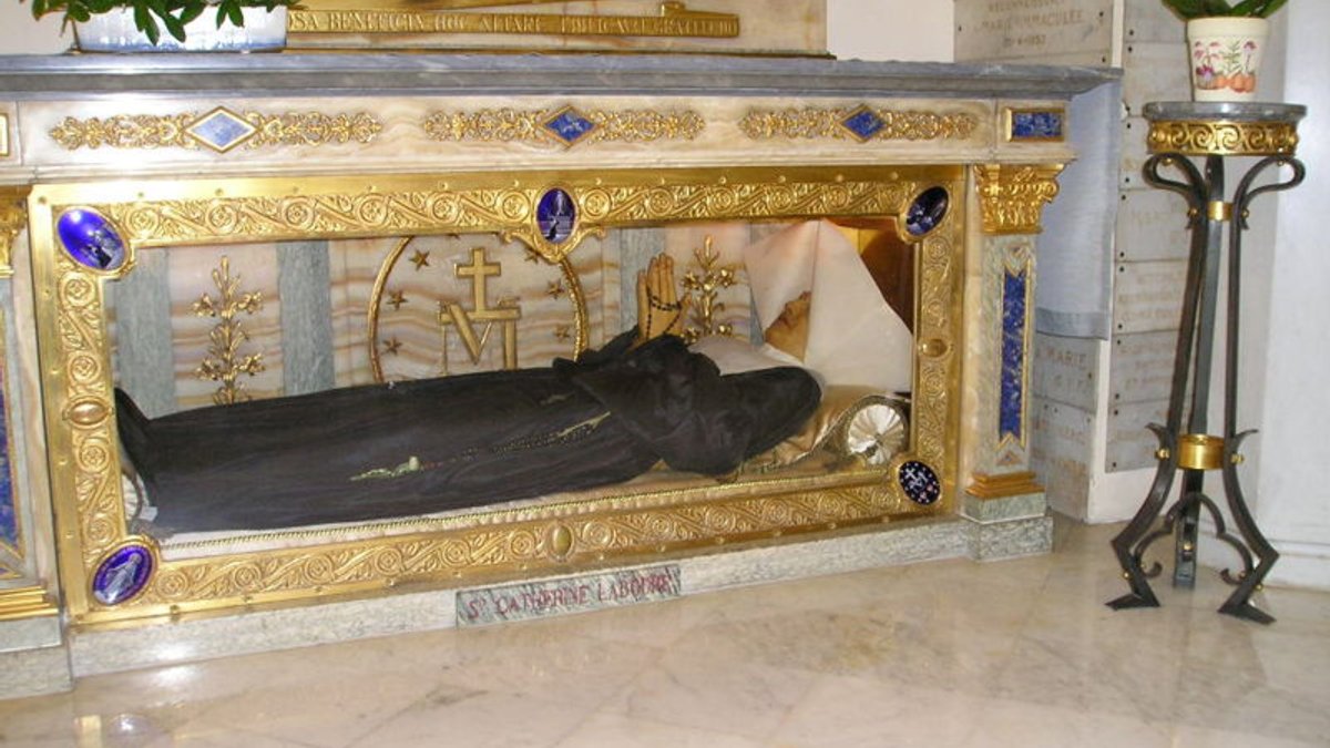 Catherine Labouré est née le 2 mai 1806 dans un petit village de Bourgogne. Alors qu’elle effectue son noviciat chez les Filles de la Charité à Paris, elle reçoit plusieurs apparitions de la vierge Marie. La deuxième est à l’origine de la diffusion de la médaille miraculeuse : le 27 novembre 1830, Catherine Labouré a deux visions qui sont par la suite représentées sur cette  médaille miraculeuse. Sur la première face de cette médaille est représentée Marie, debout sur un globe, marchant sur un serpent, les poignets cernés par des anneaux d’où jaillissent des rayons lumineux. Sur la deuxième face de la médaille un grand M (initiale de Marie) surmonté d’une croix, et en dessous deux coeurs : celui de Jésus (percé d’épines) et celui de Marie (transpercé par un glaive), le tout entouré de douze étoiles. Le corps de Sainte Catherine Labouré est exhumé le 21 mars 1933, à l’occasion de sa béatification par le pape Pie XI le 28 mai 1933. Son corps est en parfait état. Il est nettoyé et placé dans une châsse en bronze doré dans la chapelle de la Médaille miraculeuse de la rue du Bac. © André Leroux / Wikipédia