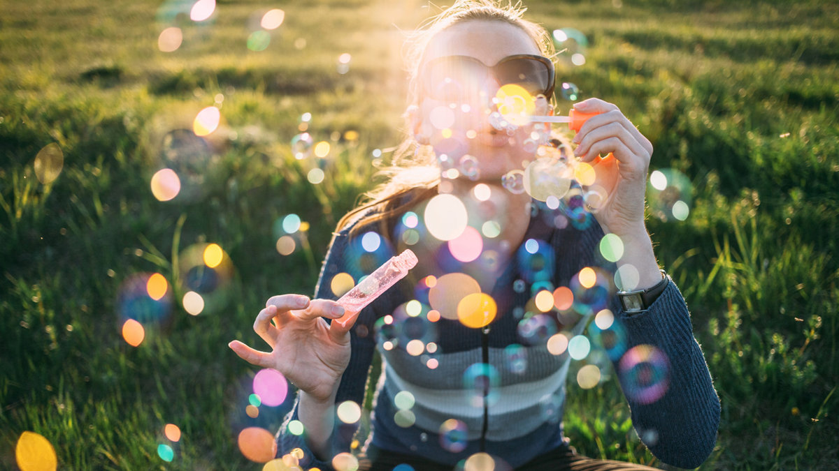 web3-woman-grass-bubbles-sunset-ilya-stocksy-united