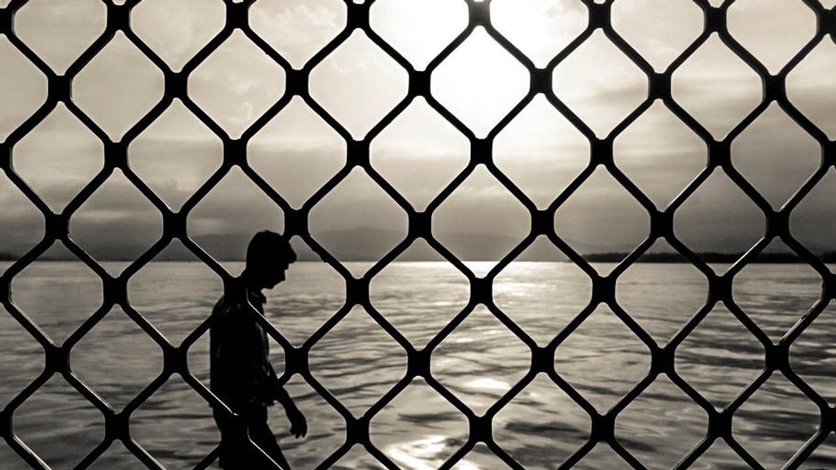 MAN WALKING ALONE BEHIND FENCE