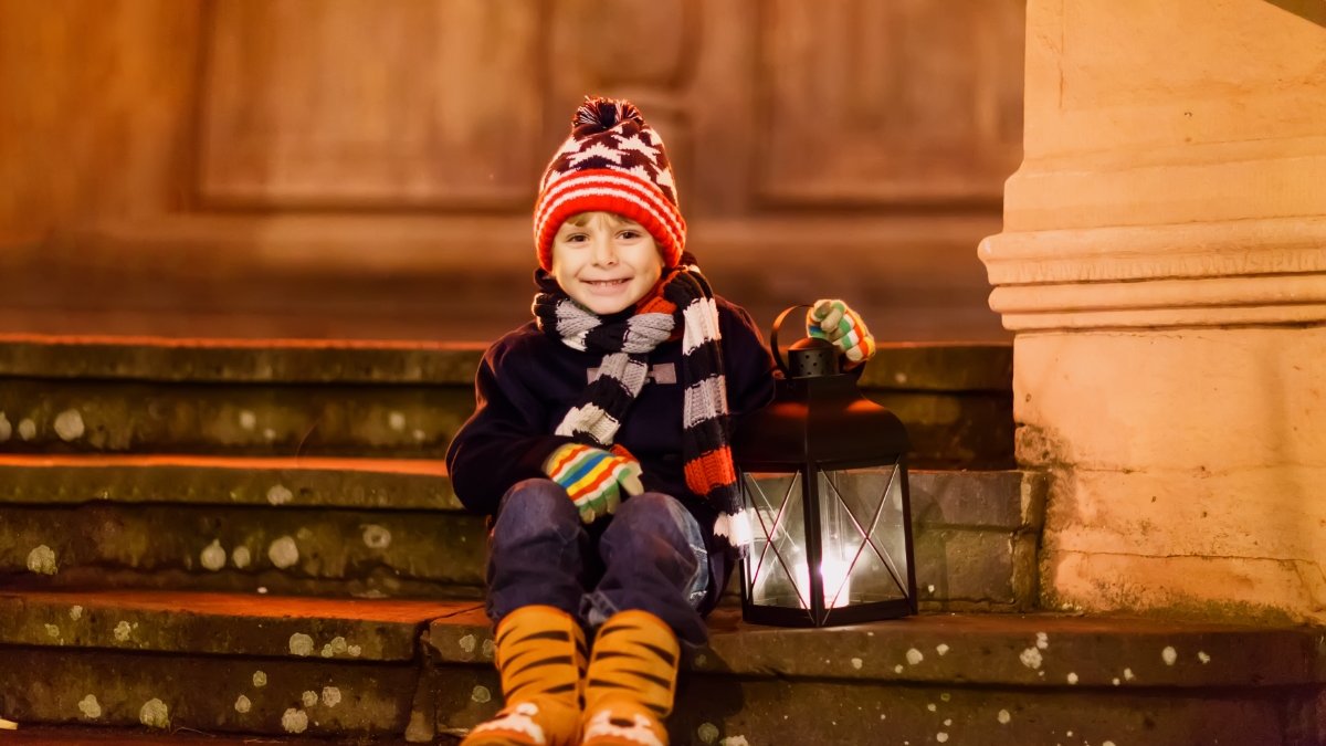 chłopiec siedzi na schodach przed kościołem i trzyma lampion adwentowy