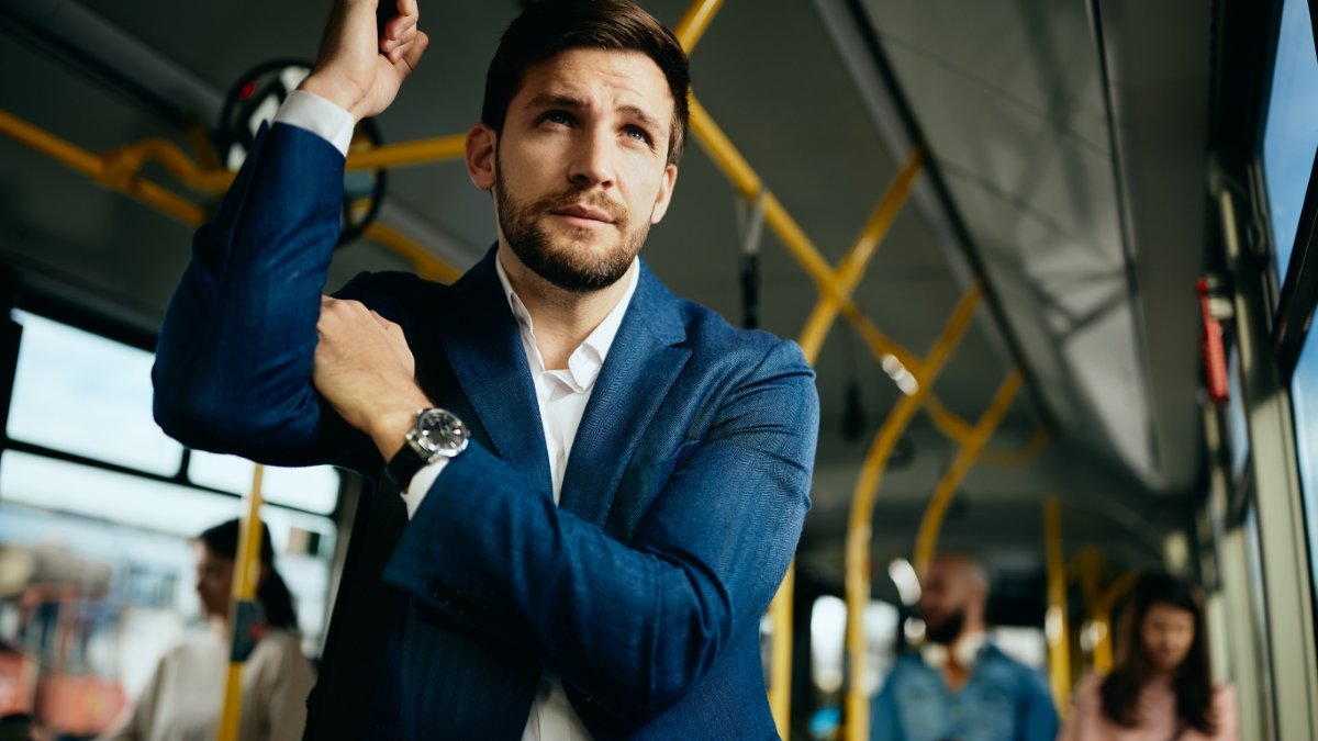mężczyzna ubrany w garnitur stoi w autobusie jadąc do pracy i patrzy w dal przez okno