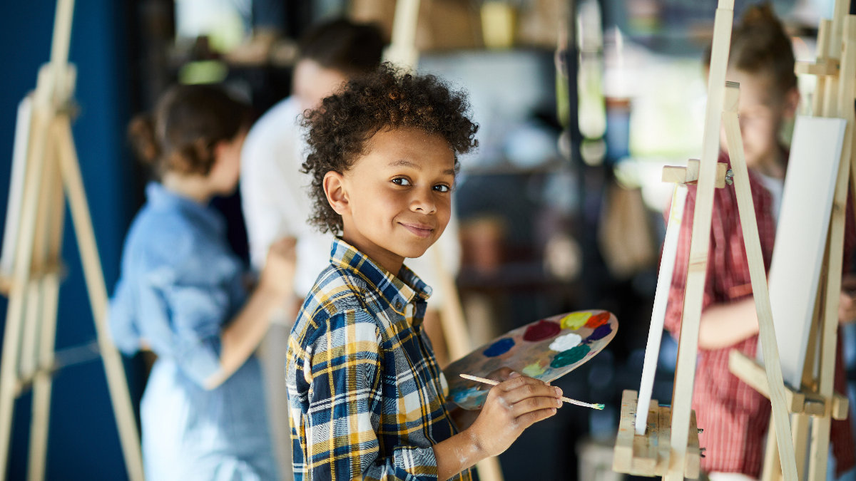 Young boy with color palette standing by easel painting