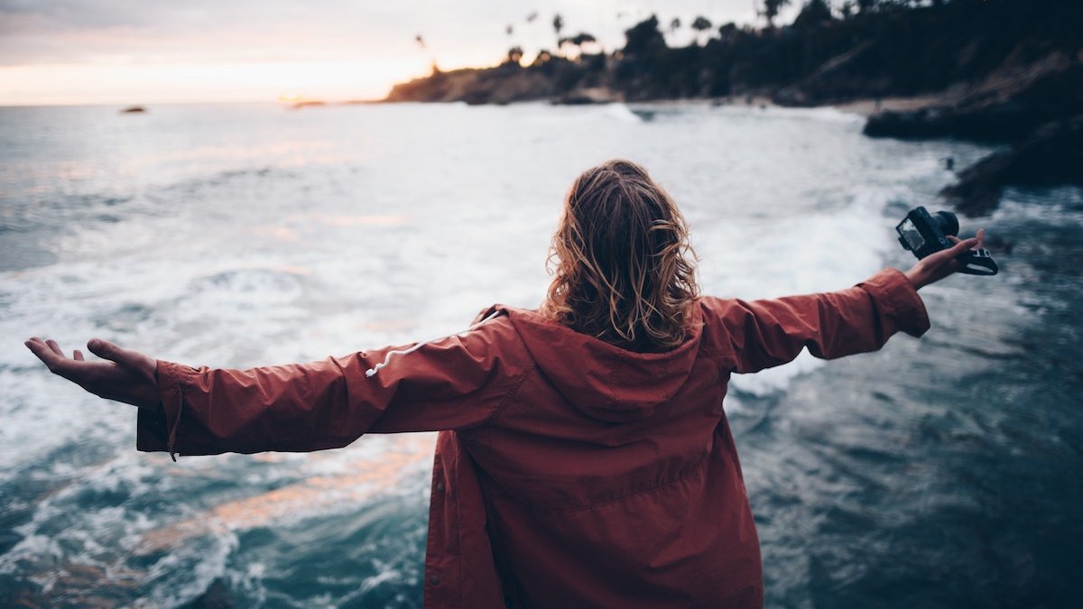 a girl with her arms outstretched stands on the beach and looks at the sea