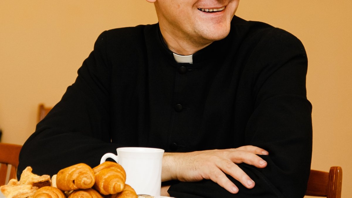 Ksiądz zaproszony do domu rozmawia przy stole z członkami rodziny