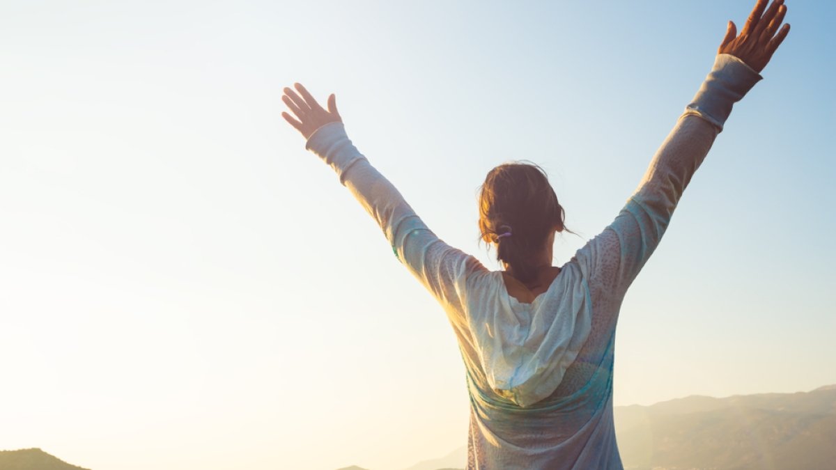 Happy traveler, woman with open arms stands on the rock