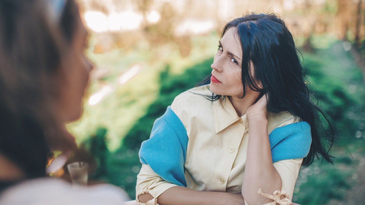 Woman with an indignant look looks at her friend sitting at a round table in a cafe