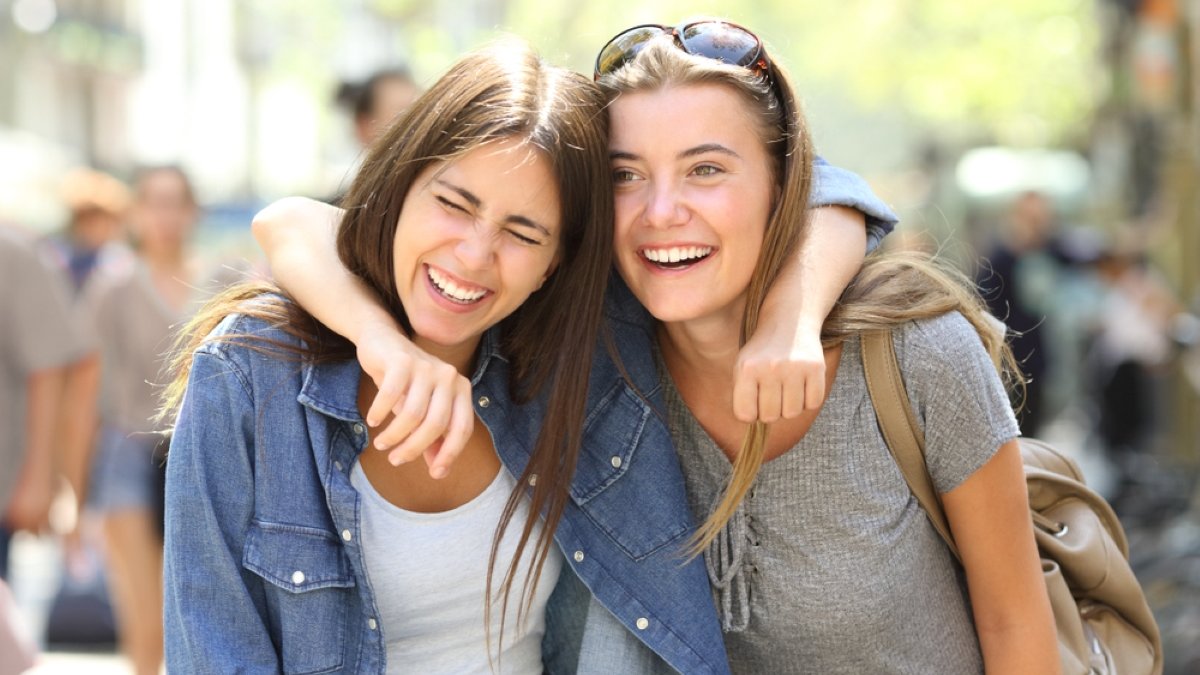 Two funny friends laughing loud walking in the street