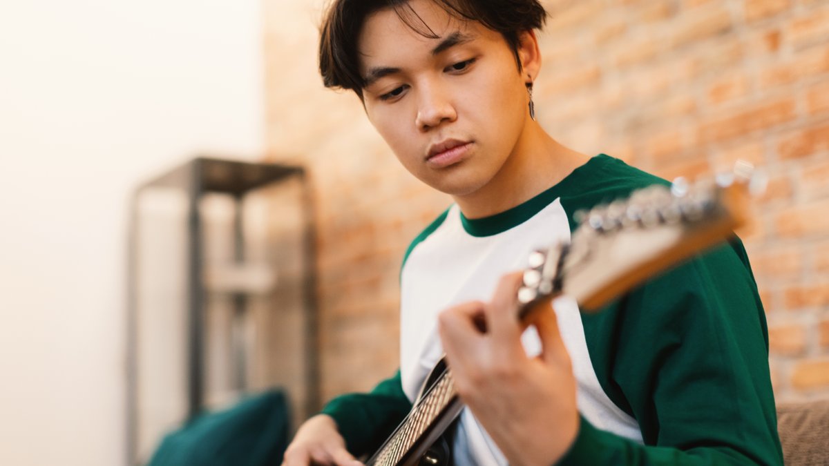 Un-Adolescente-Japones-Tocando-Guitarra-Electrica-Tocando-Cadenas-Tomando-Coros-Sentados-En-Sofa-En-Casa.-shutterstock_2280495105.jpg