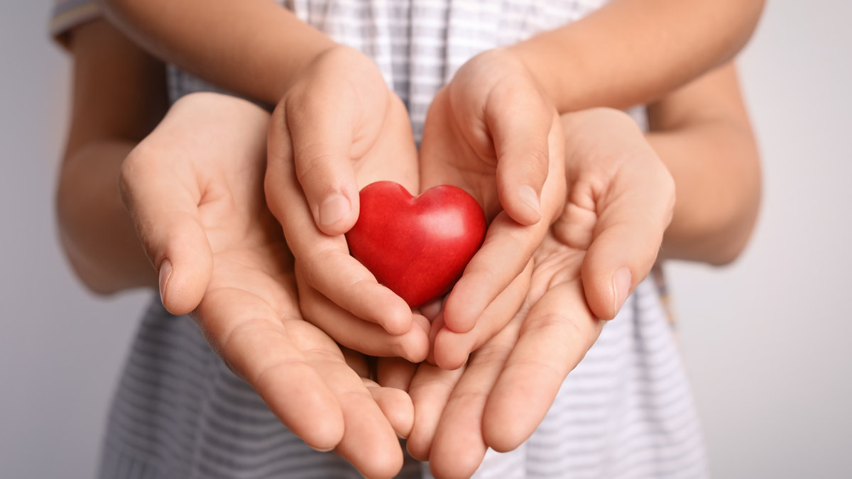 Familia-agarrando-el-pequeno-corazon-rojo-en-las-manos-cerrando-shutterstock_1153562026.jpg