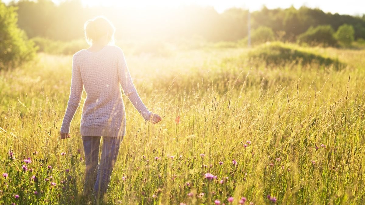 Woman standing in a field facing away from the camera towards the sun