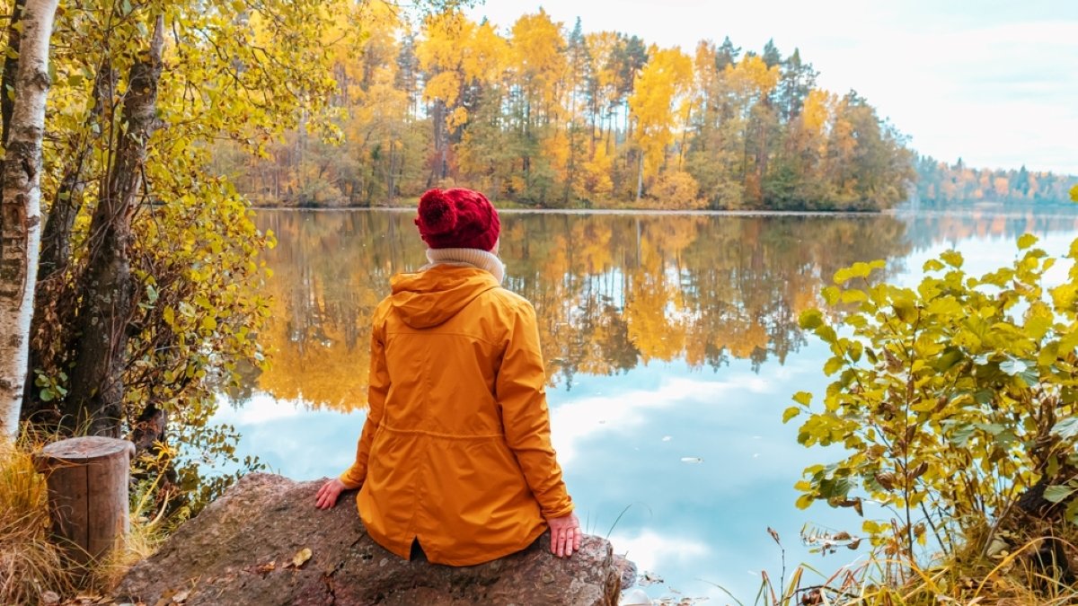 Lonely woman is sitting on the shore of a forest lake