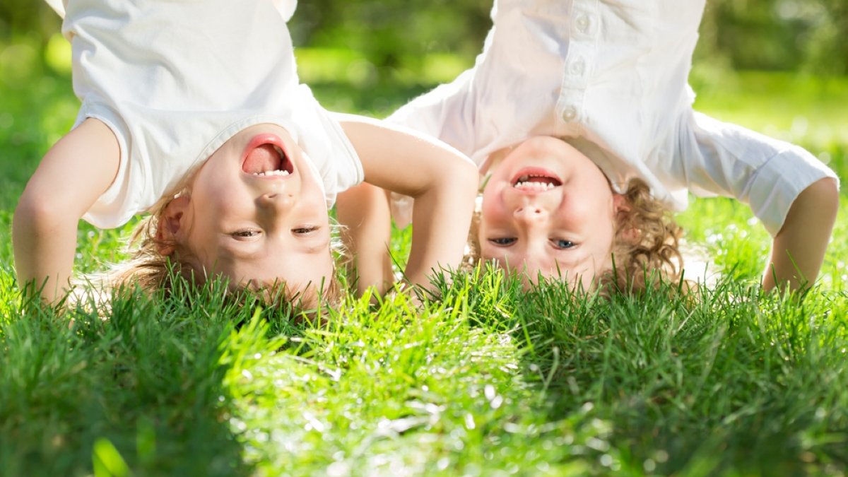 Happy children playing head over heels on green grass in spring park