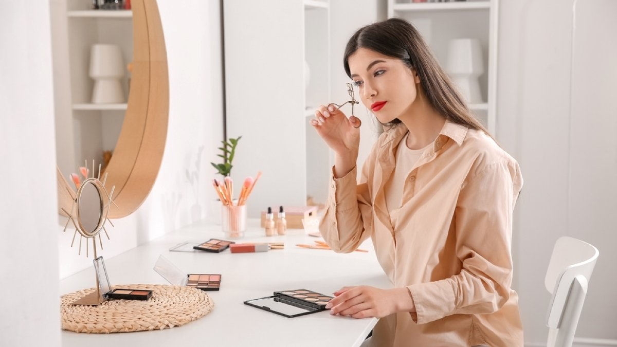 Beautiful young woman curling eyelashes in dressing room