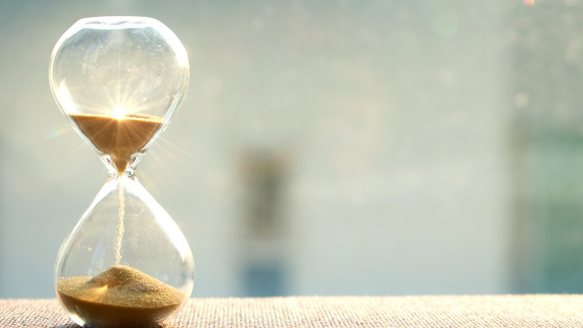 Life time passing concept. Hourglass with sun light background