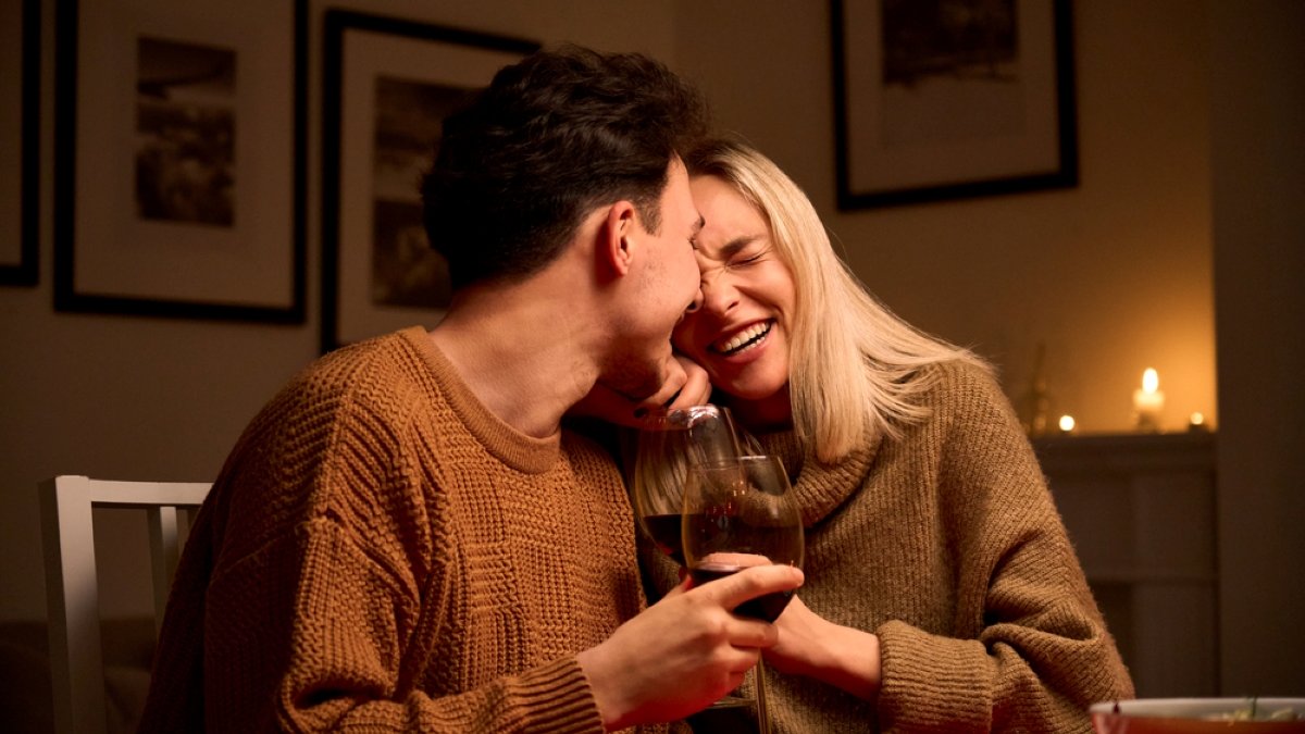 Happy young couple in love hugging, laughing, drinking wine, enjoying talking