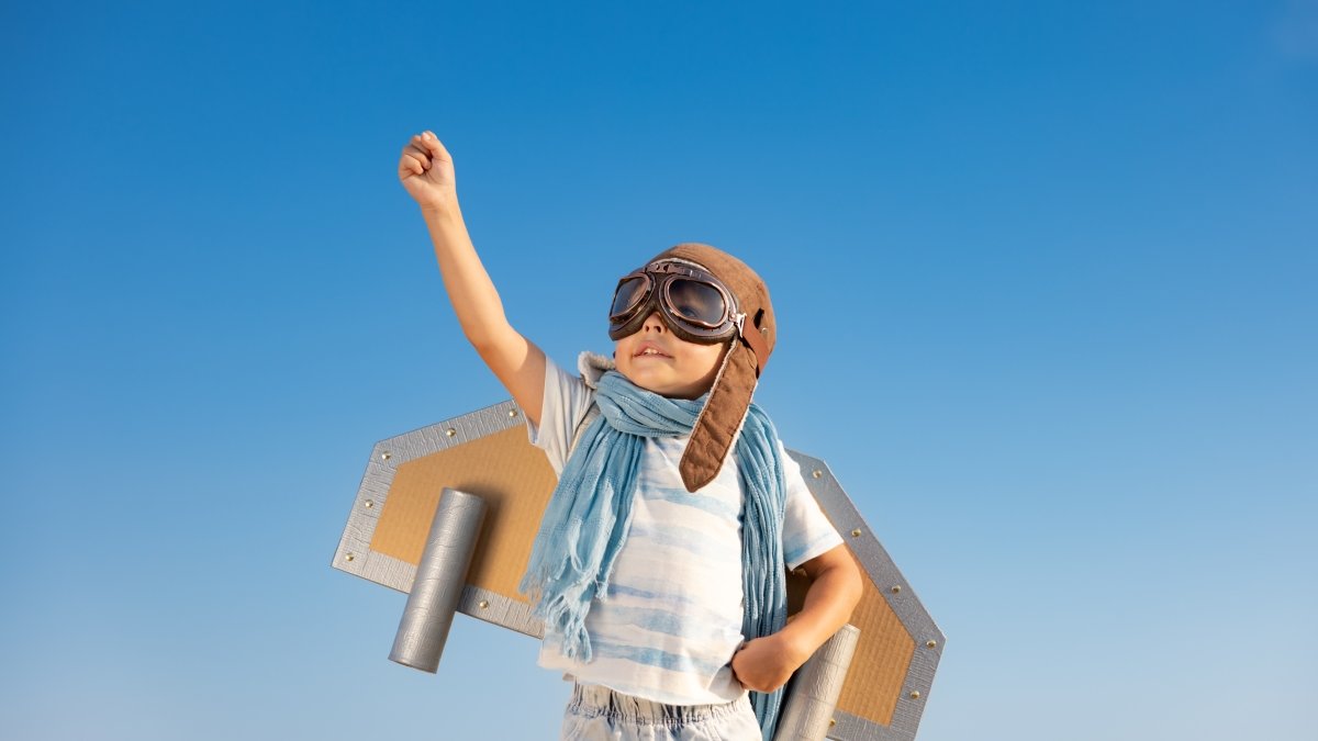 Happy child playing with toy wings against blue sky background