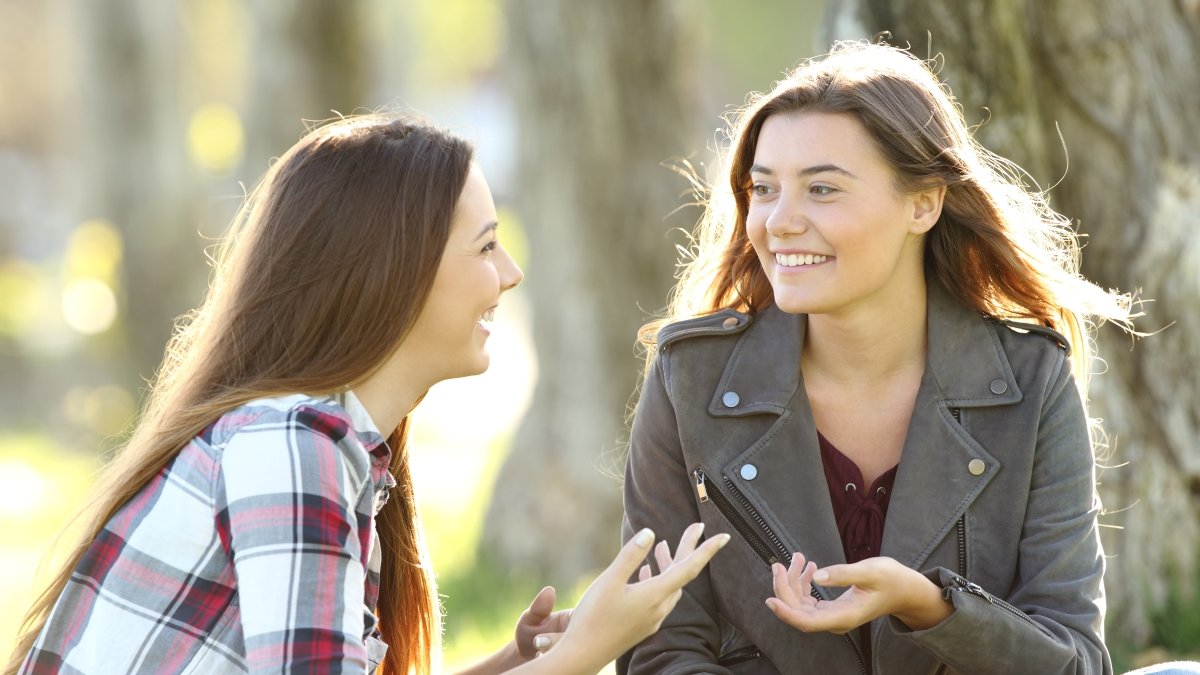 Two friends talking and laughing sitting on the grass in a park
