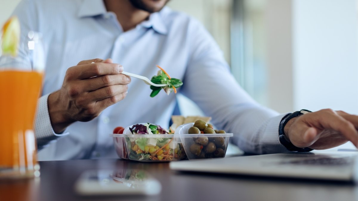 Close-up of businessman eating healthy food while using computer on lunch break in the office