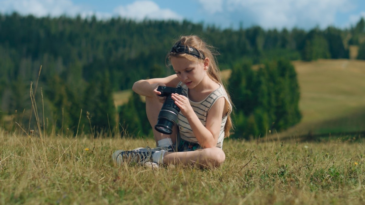Young photographer watching results of work, sitting on mild grass hill