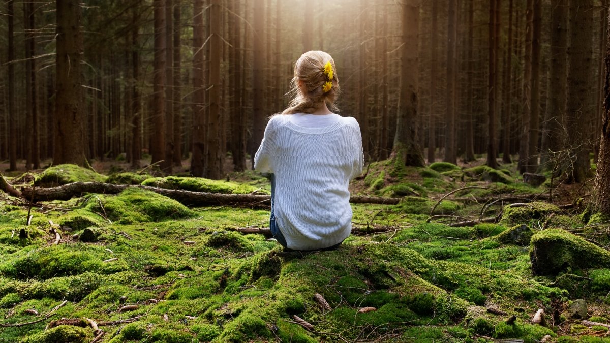 Woman sitting in forest enjoys the silence and beauty of nature