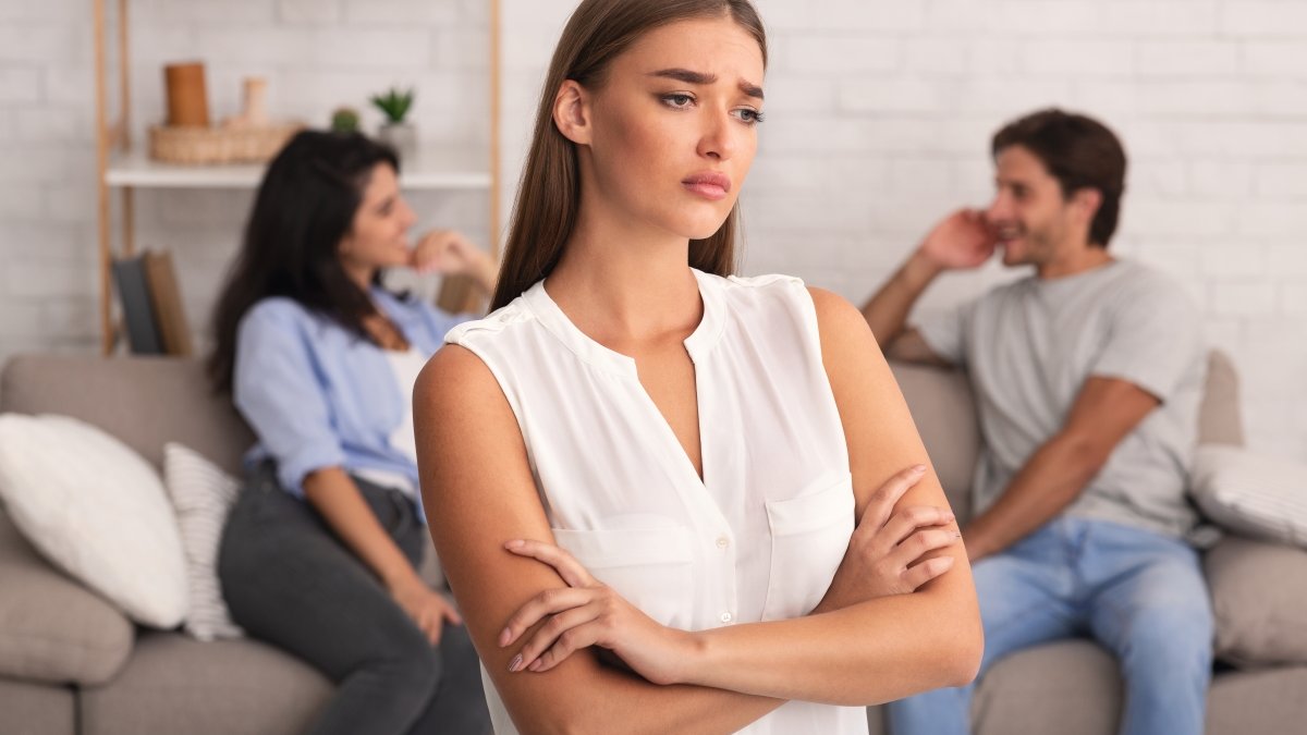 Jealous woman standing with back to couple on sofa