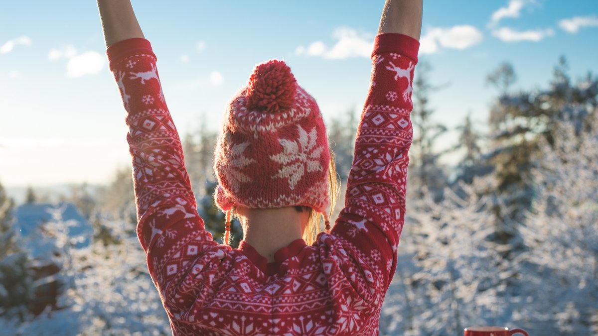 Woman in pink sweater and knit hat raising hands from back winter scene