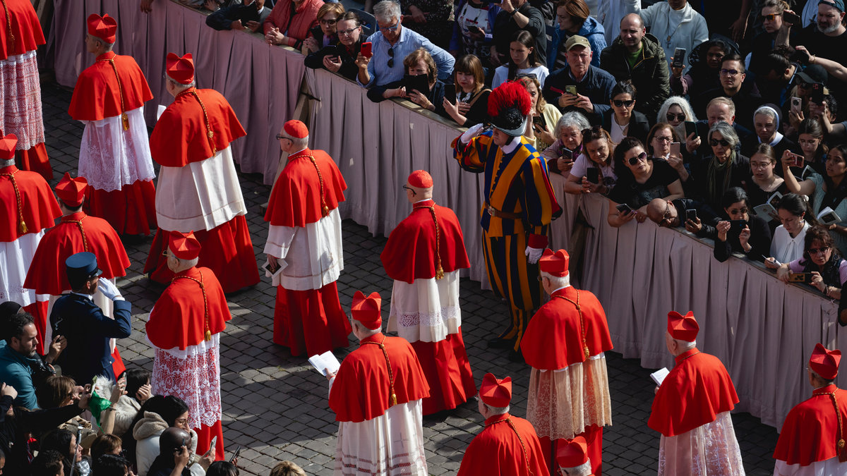 Members of the clergy march next to attendees prior to the arrival of the coffin of the late Pope, set to be transported from the chapel of Santa Marta to St Peter's Basilica, following the Pope's death, in the Vatican on April 23, 2025.