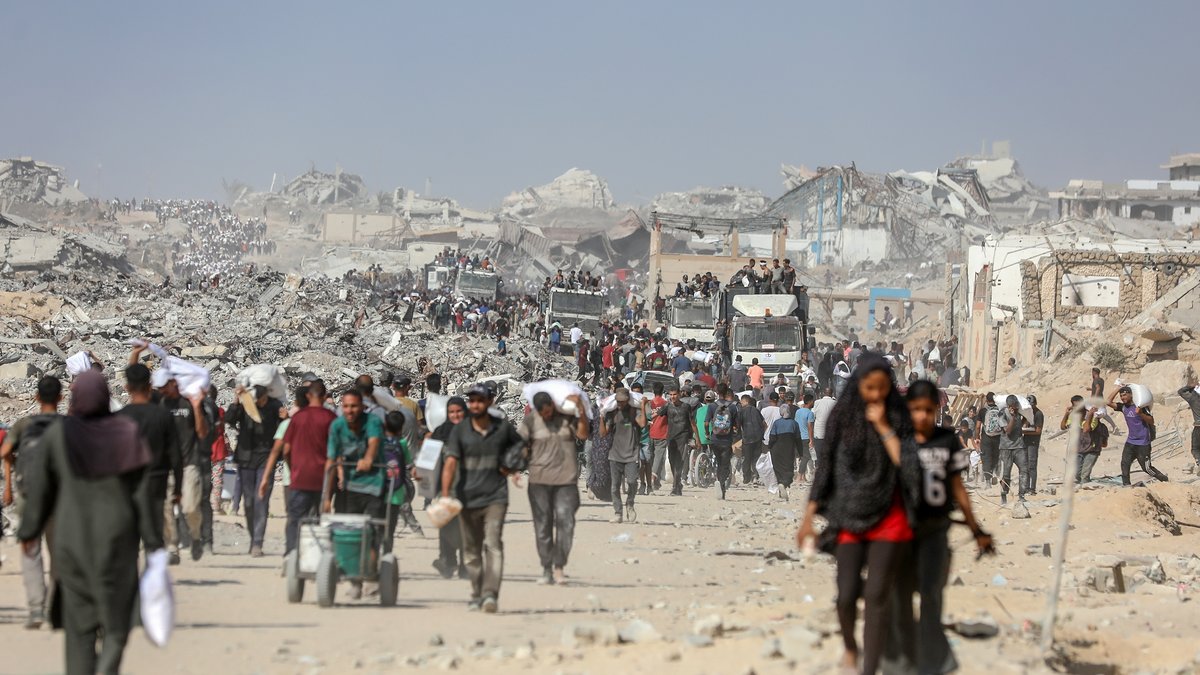 Palestinians carry flour and food aid they received at the Zikim crossing in the central Gaza Strip, August 8, 2025