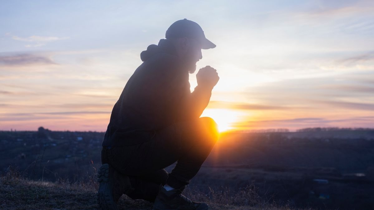 Prayer. Man on his knees praying. On the background of the sunset sky. Kneeling Prayer to God. Worship and praise.