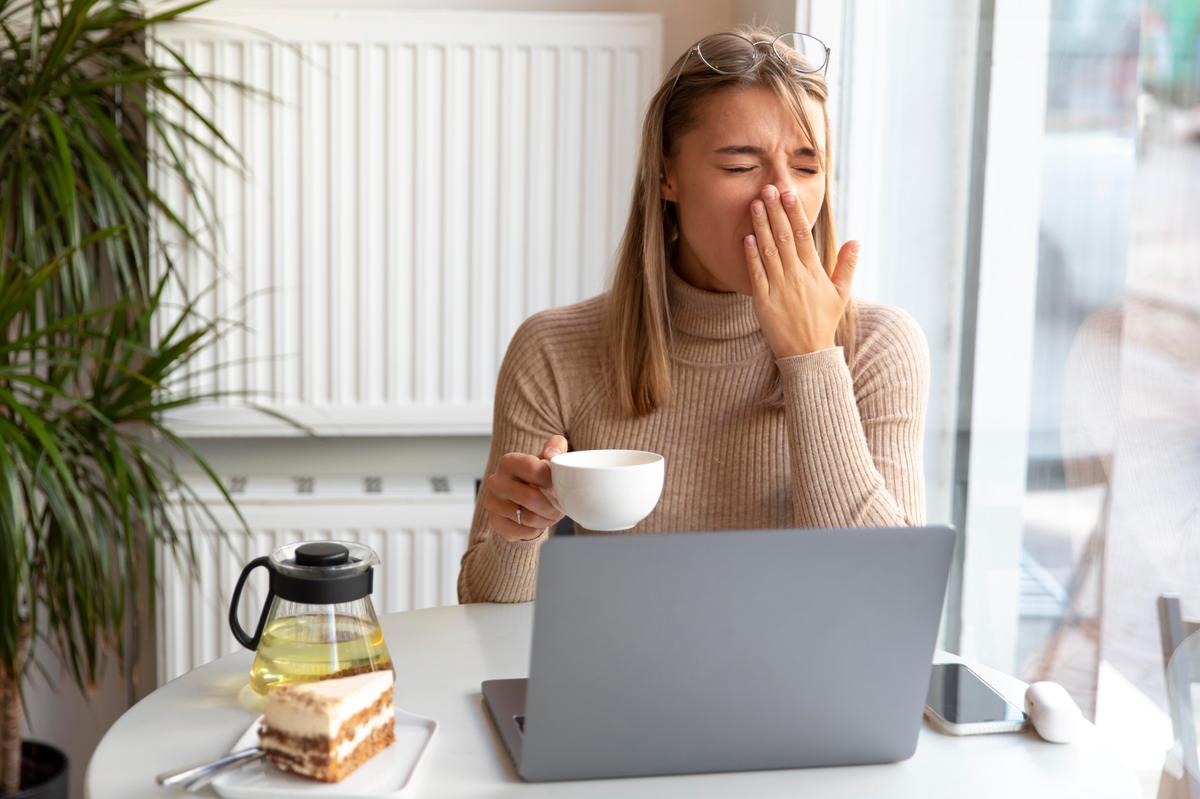 a-woman-at-her-desk-at-work-drinks-her-tea-while-yawning