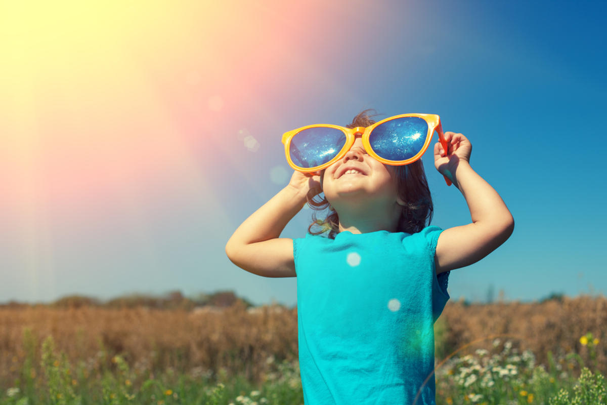 Happy little girl with big sunglasses walking in the meadow and looking at the sun