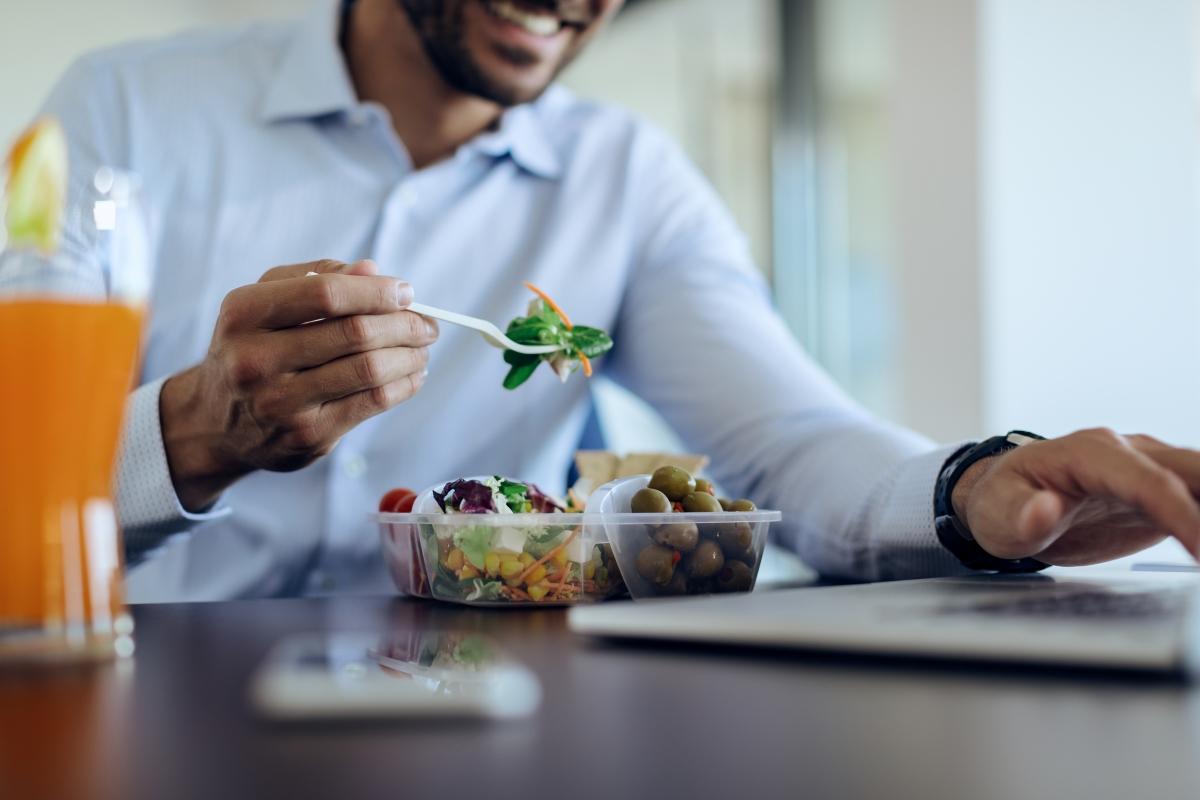 Close-up of businessman eating healthy food while using computer on lunch break in the office