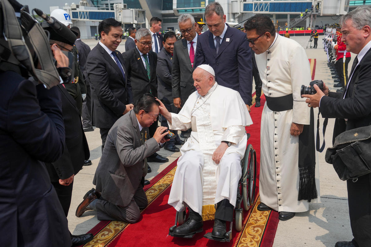 A man kneels before Pope Francis (C) upon his arrival for a farewell at Jakarta's Soekarno-Hatta International Airport ahead of his departure to Papua New Guinea's capital Port Moresby on September 6, 2024.