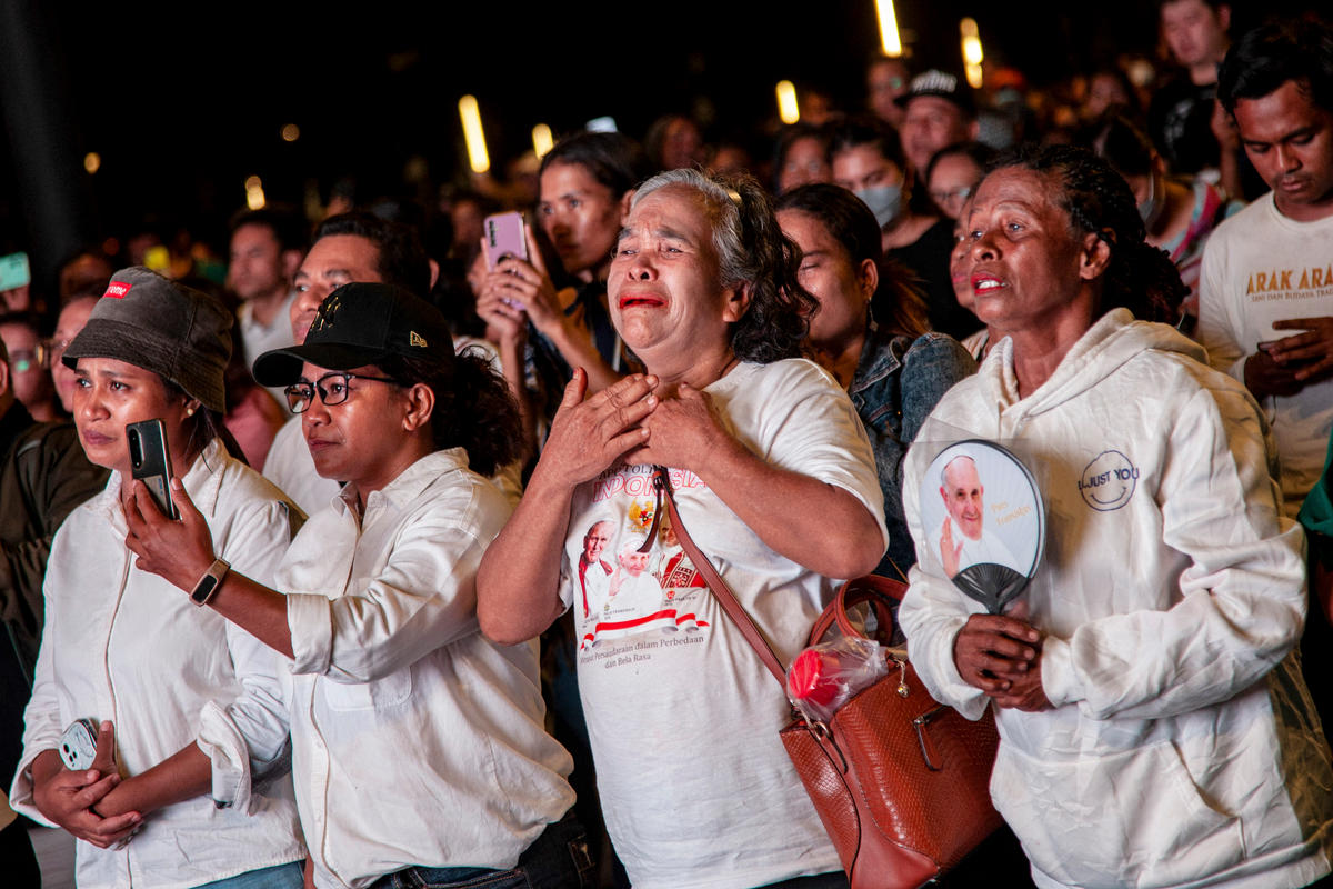 Catholic faithfuls react as they watch an electric screen, live streaming the holy mass led by Pope Francis, outside the Gelora Bung Karno Stadium in Jakarta on September 5, 2024.