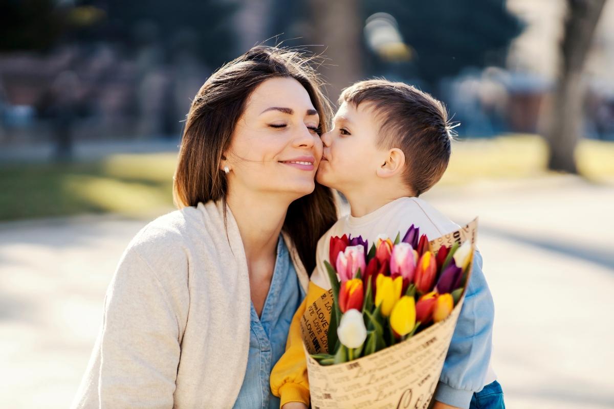 A little boy giving bouquet of tulips to his mother and kissing her on mother's day