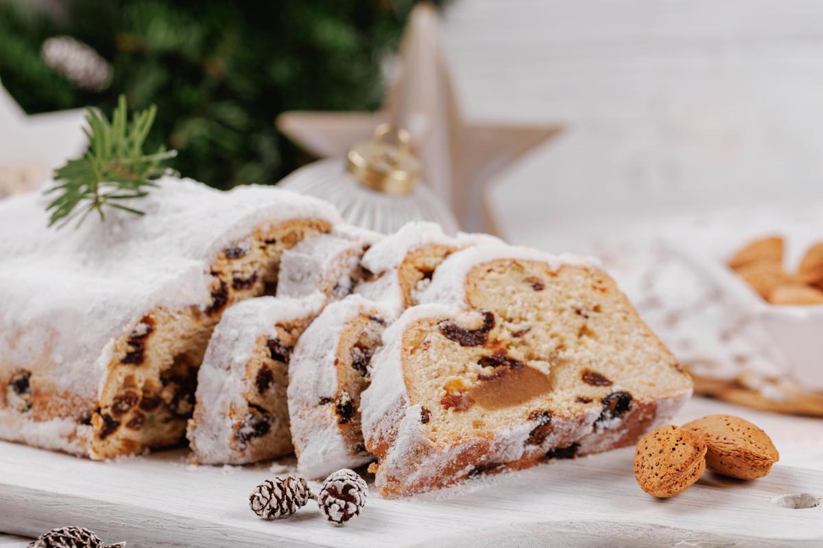 Christmas stollen loaf with a sugar coating, sliced and displayed with almonds, pinecones, and festive ornaments, capturing the spirit of the holiday season.