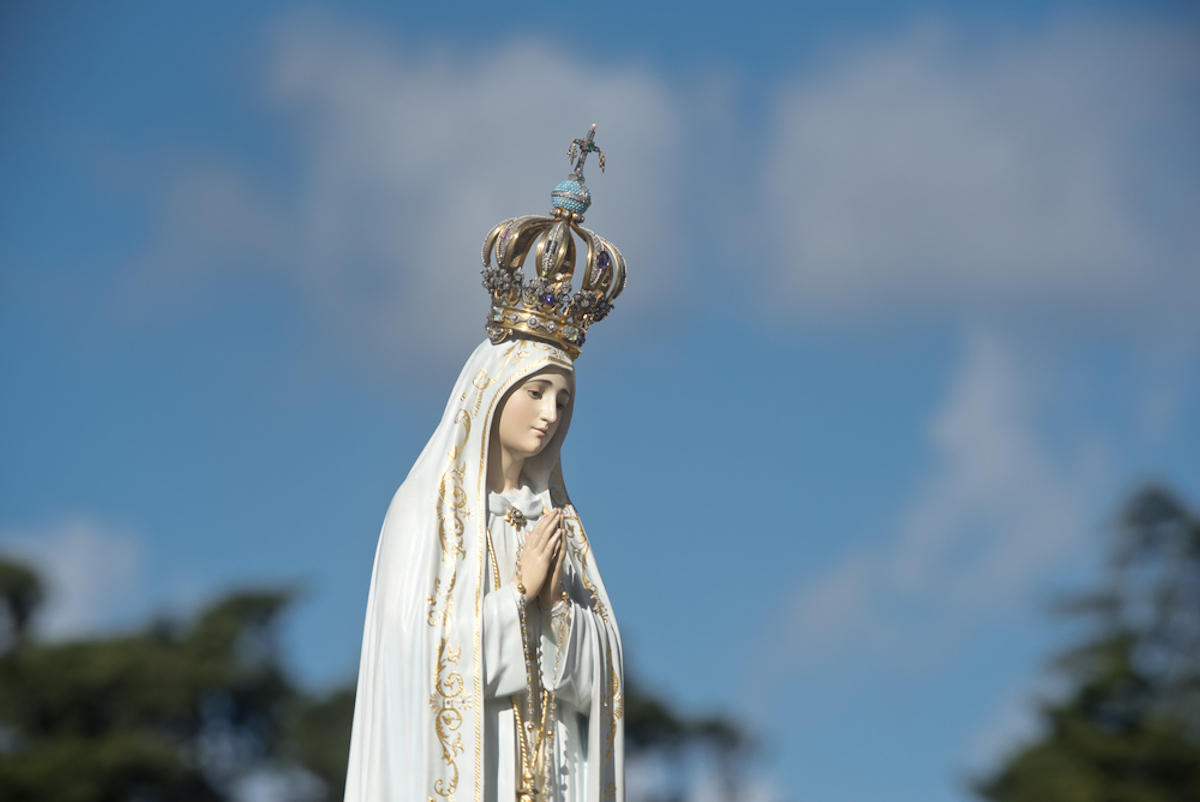 Estátua de Nossa Senhora de Fátima sob o céu azul com nuvens
