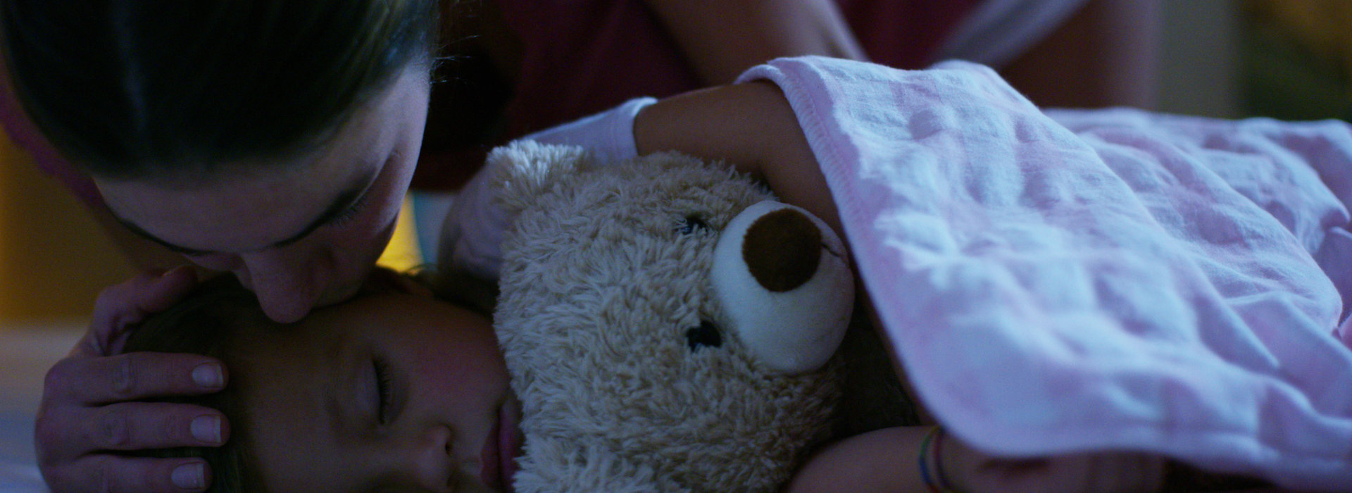 mother tucking in child with teddy bear
