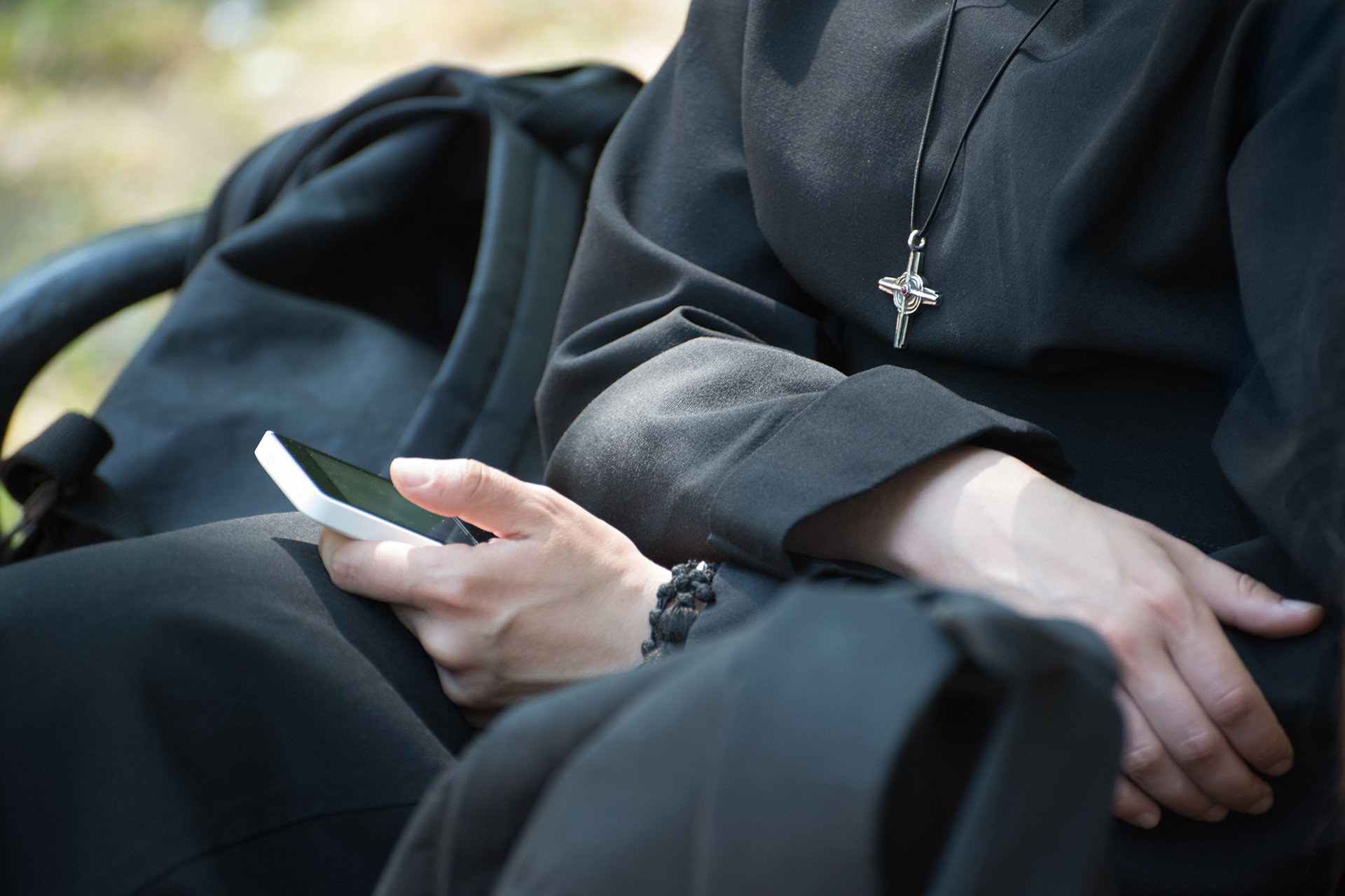 Unrecognizable-nun-in-a-black-robe-with-a-cross-on-his-neck-uses-a-smartphone-