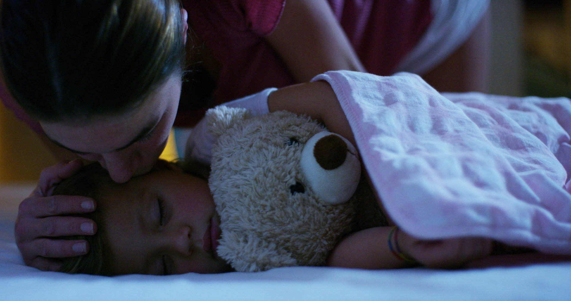 mother tucking in child with teddy bear