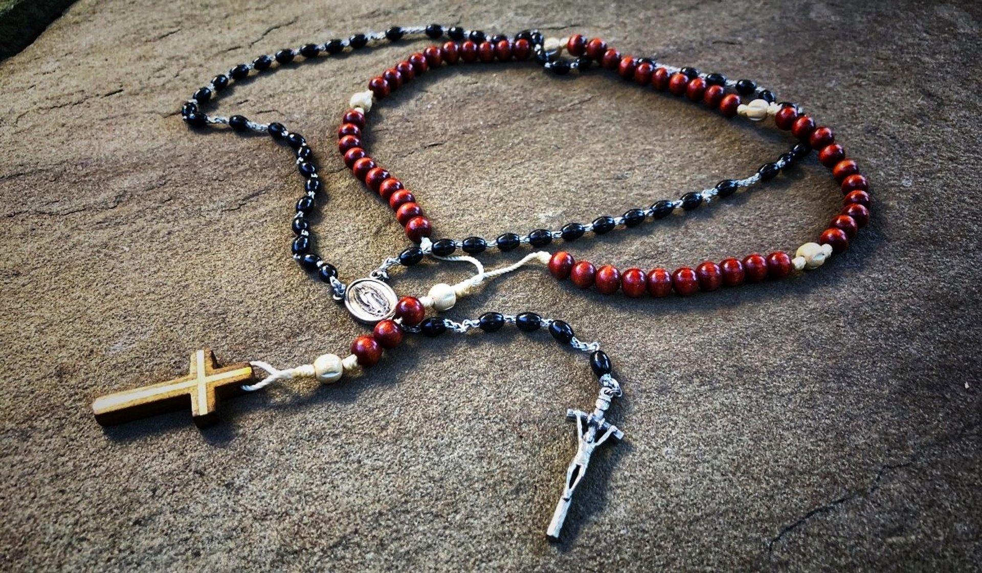 Two entwined rosaries, one black and one brownish red, placed on a slab of granite.