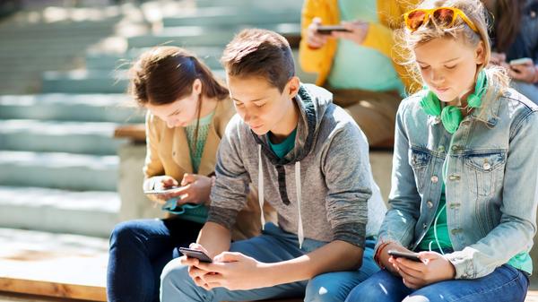 grupa nastolatków siedzi na schodach i wpatruje się w smartfony