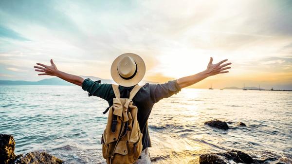 Happy man raising arms up enjoying sunset on the beach