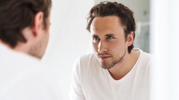 Attractive confident young man standing in front of the bathroom mirror