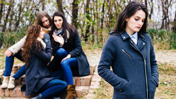 Sad-girl-with-friends-gossiping-in-background-behind-her-back-shutterstock